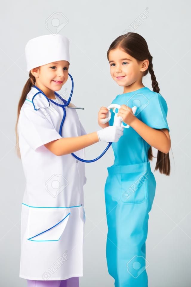 Little girl in doctor costume do listening another girl s lungs, playing with stethoscope, isolated on white