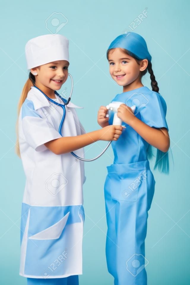 Niña en traje de médico no escucha los pulmones otra chica s, jugando con el estetoscopio, aislado en blanco
