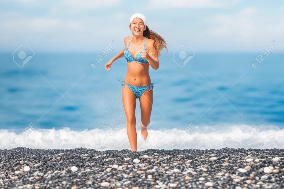Happy young girl running from sea on beach with pebbles