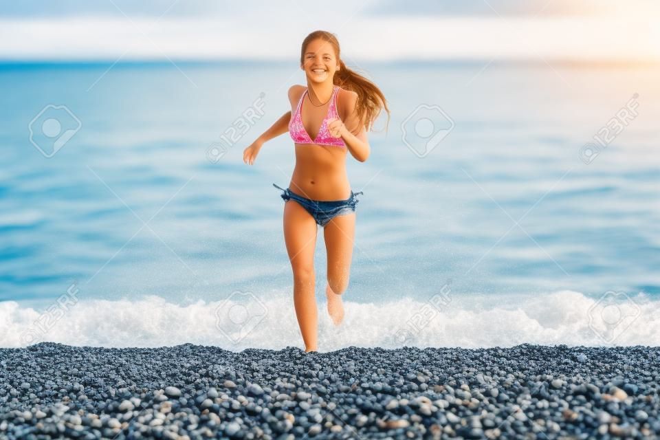 Happy young girl running from sea on beach with pebbles