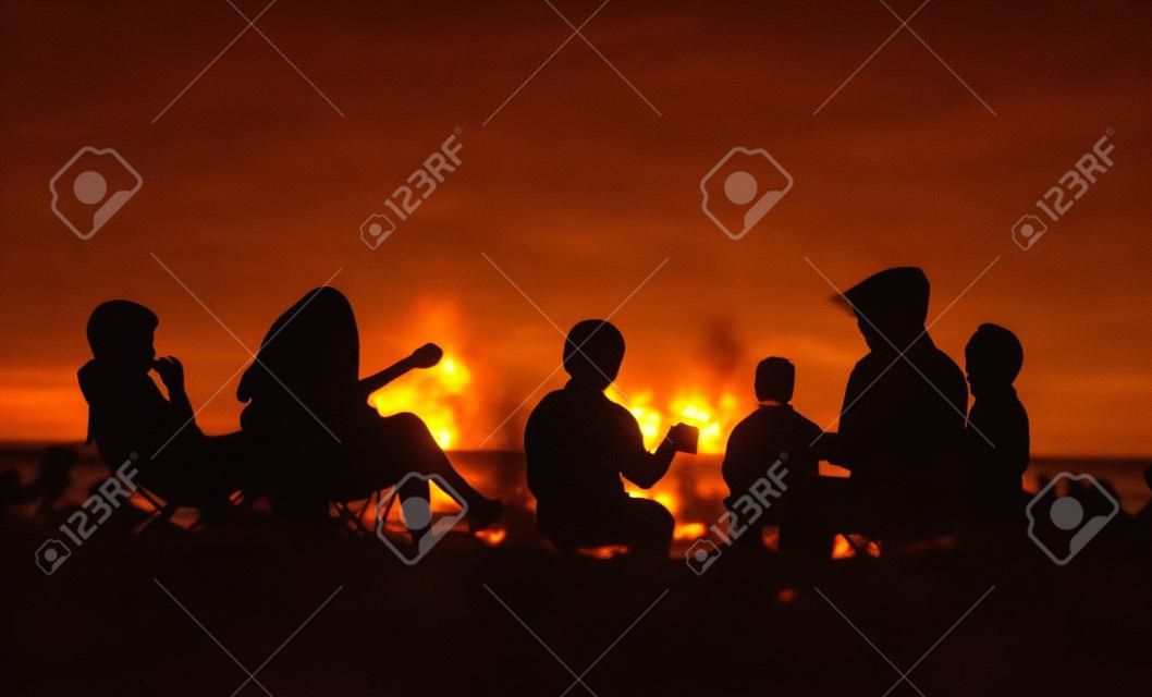 Silhouette of people sitting on the beach with campfire at sunse