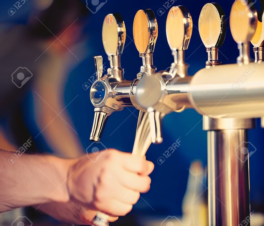 Barman hand at beer tap pouring a draught lager beer serving in a restaurant or pub.