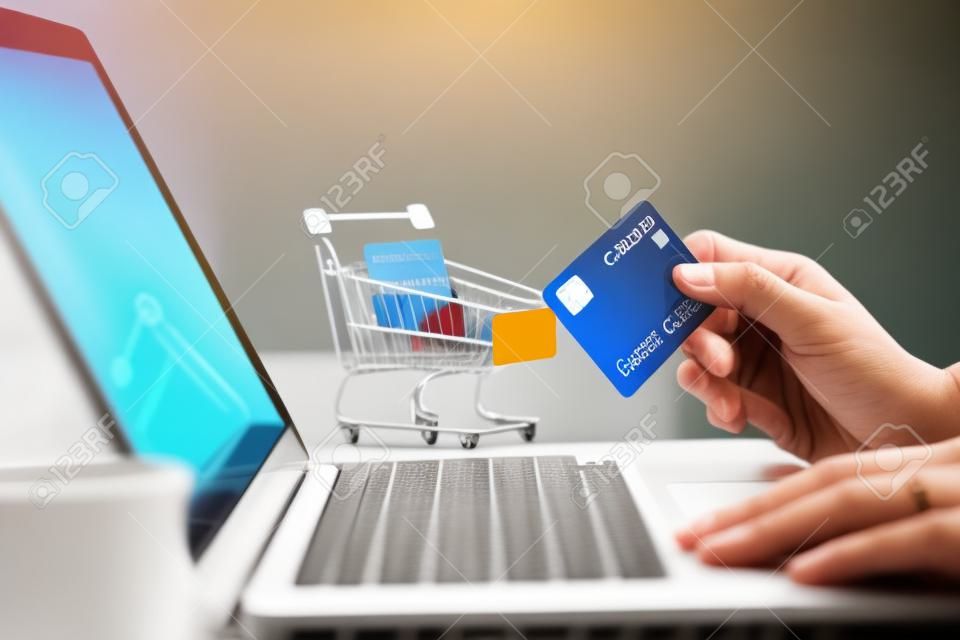 Hands holding credit card and using laptop computer with shopping cart background. Online shopping, E-payment or internet banking