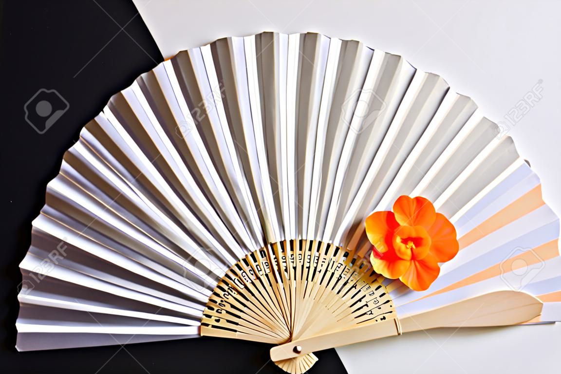 decorative white hand fan with a wooden grip and an orange colored blossom on black and white paper