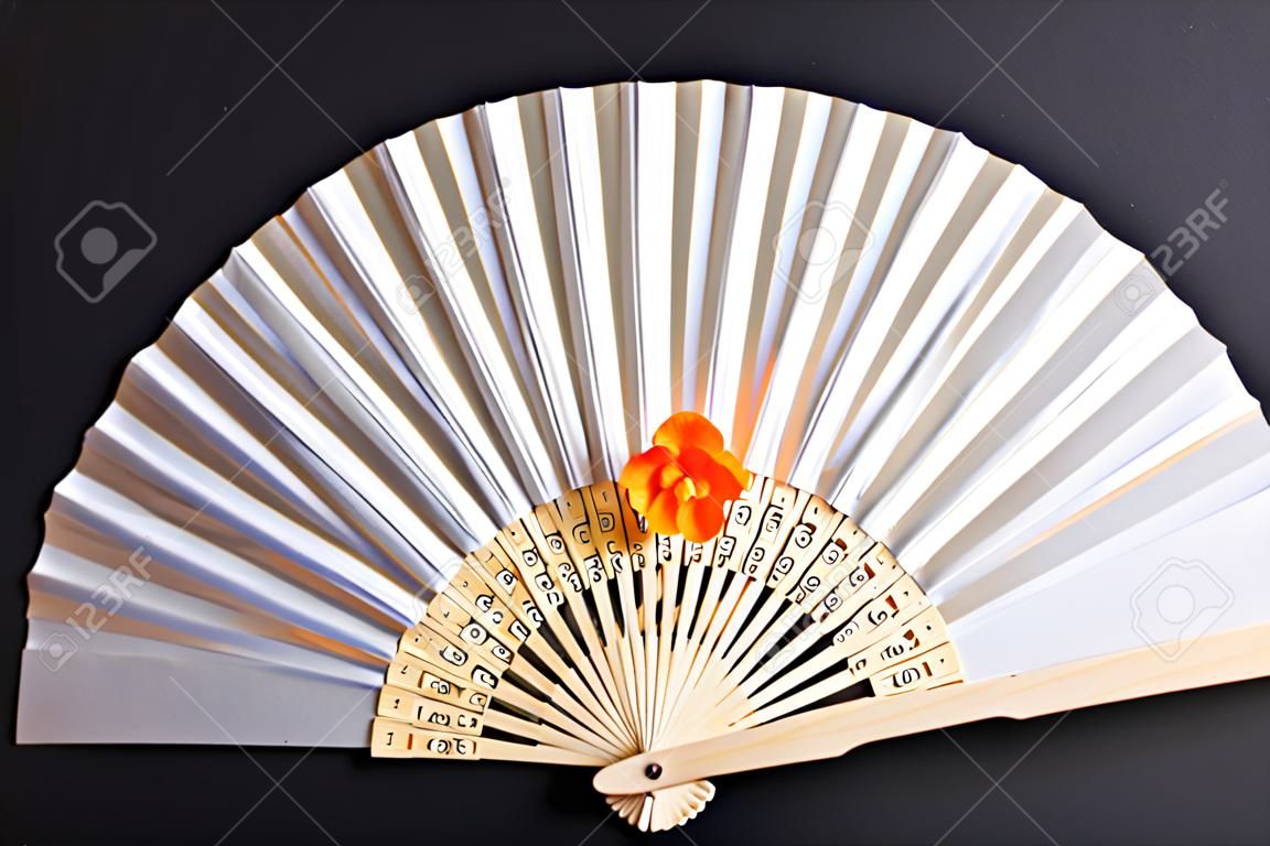 decorative white hand fan with a wooden grip and an orange colored blossom on black and white paper