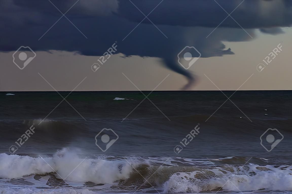 A hurricane is about to batter this caribbean beach . The seas are raging and the skies show the tropical storm as the power of nature is demonstrated. Waves crash on the shore.