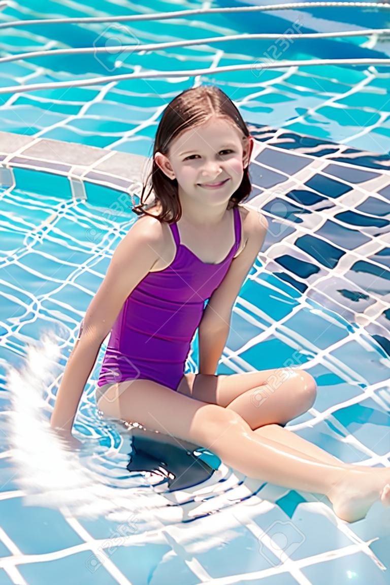 Cute smiling preteen girl sitting at swimming pool edge. Travel, vacation, childhood concept