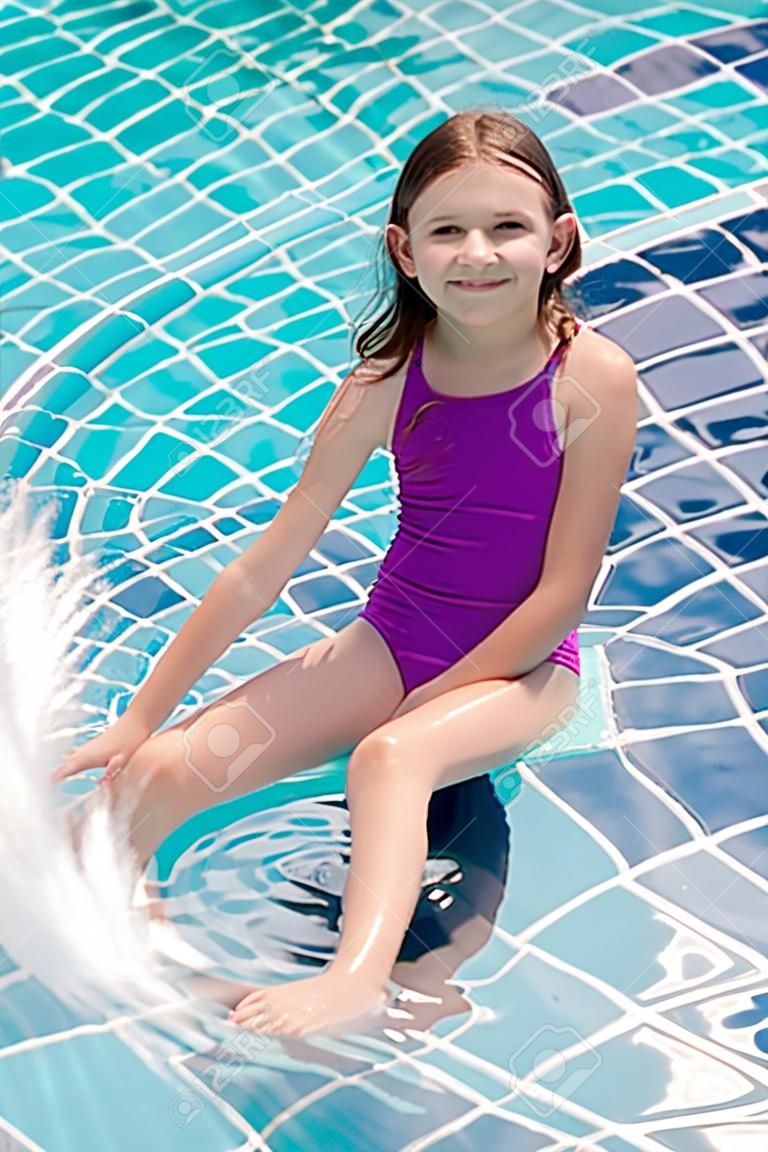 Menina pré-adolescente sorridente bonito que senta-se na borda da piscina. Viagem, férias, conceito da infância
