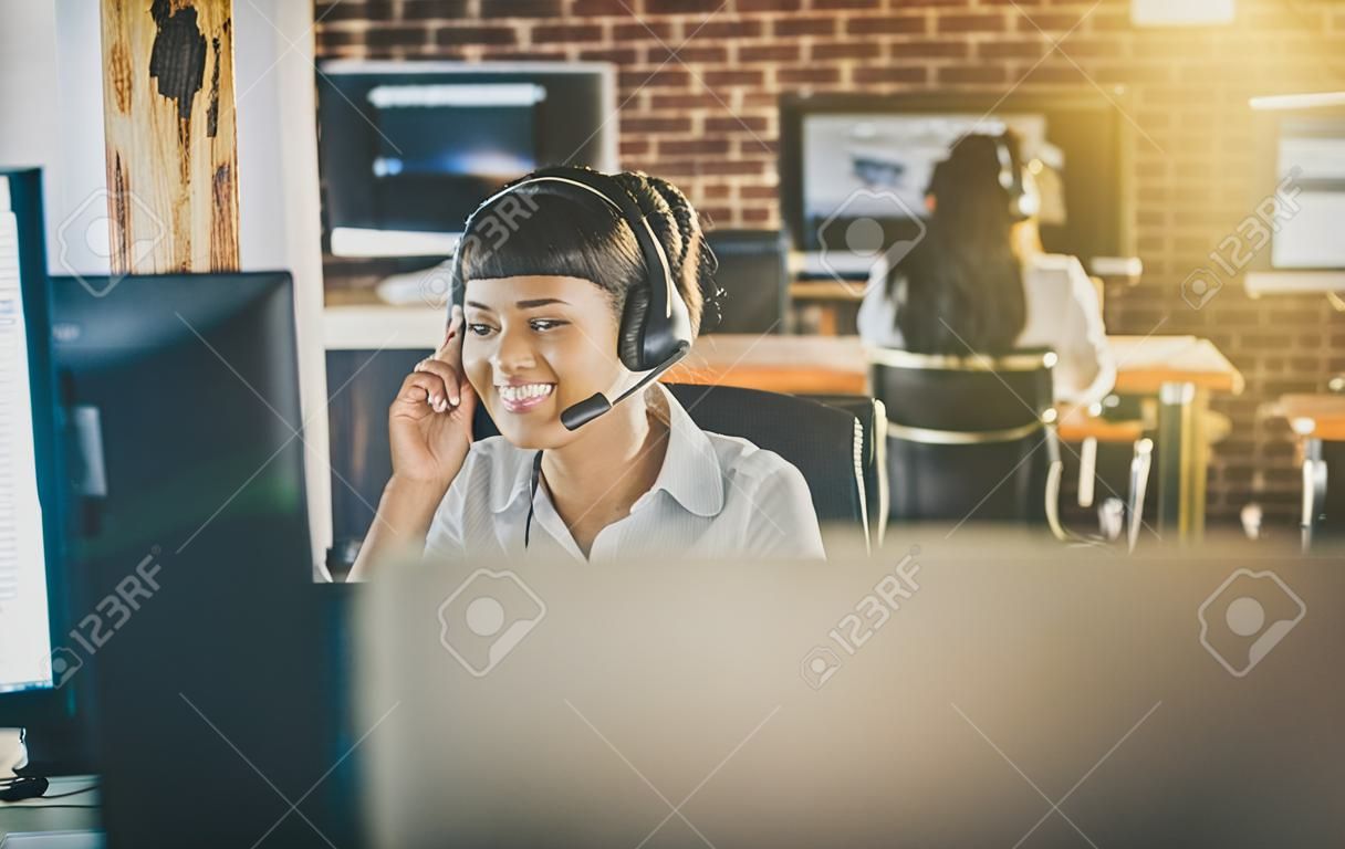 呼叫中心工作人員在其團隊的陪同下。微笑的客戶支持運算符在工作。年輕僱員與耳機一起使用。
