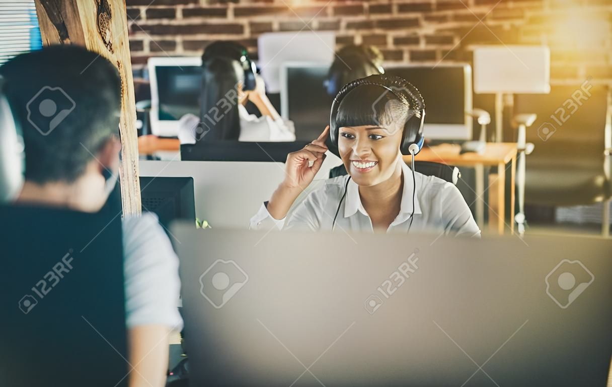呼叫中心工作人员在其团队的陪同下。微笑的客户支持运算符在工作。年轻雇员与耳机一起使用。