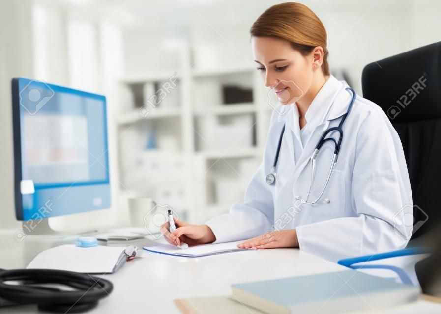 Ernste erwachsene Frau Doktor mit Stethoskop auf ihren Schultern Schreiben einige medizinische Ergebnisse auf ein Papier an ihrem Arbeitstisch.