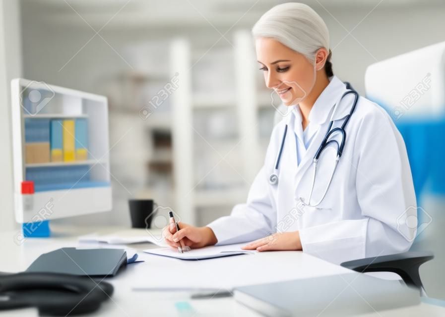 Onun tezgahının bir Kağıda Bazı Tıbbi Bulgular Yazma onu Omuzlar üzerinde stetoskop ile ciddi Yetişkin Kadın Doktor.