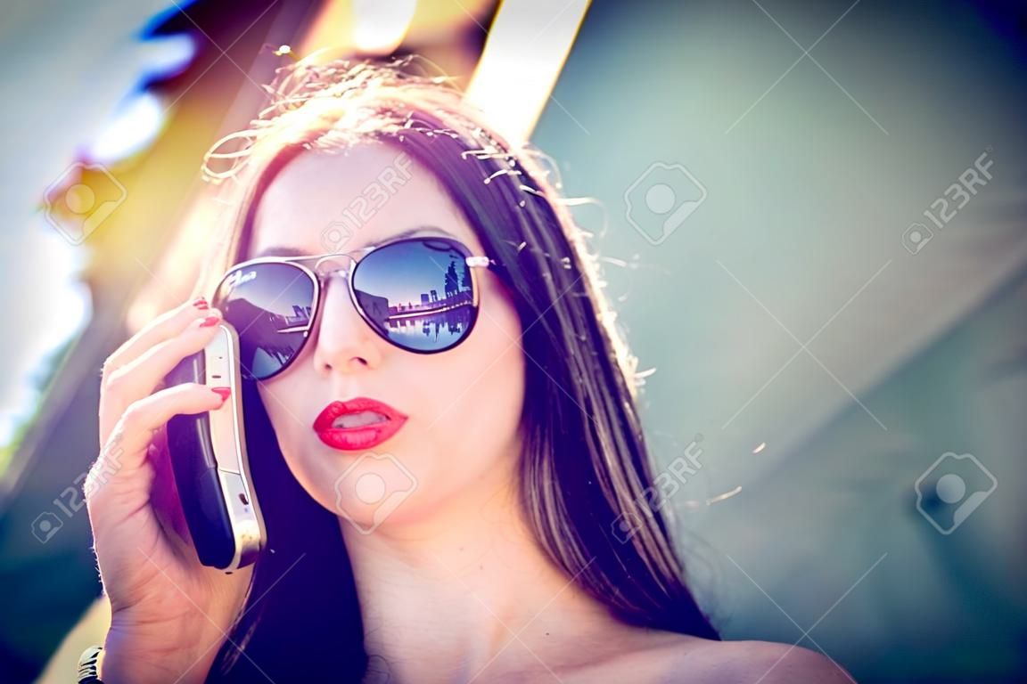Attractive spontaneous woman talking on the phone. Authenticity and Spontaneity. Authentic conversation over the phone. The girl in sunglasses holds a mobile phone in hand.