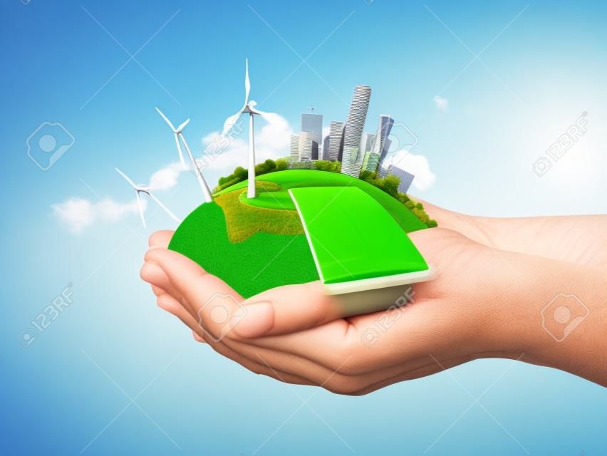 Manos sosteniendo prado verde claro con el bloque de batería solar, turbinas de viento molino y el concepto de ciudad de los rascacielos de la ecología, la creciente colección de negocio, la frescura, la libertad y otras cuestiones de estilo de vida los campos de verde