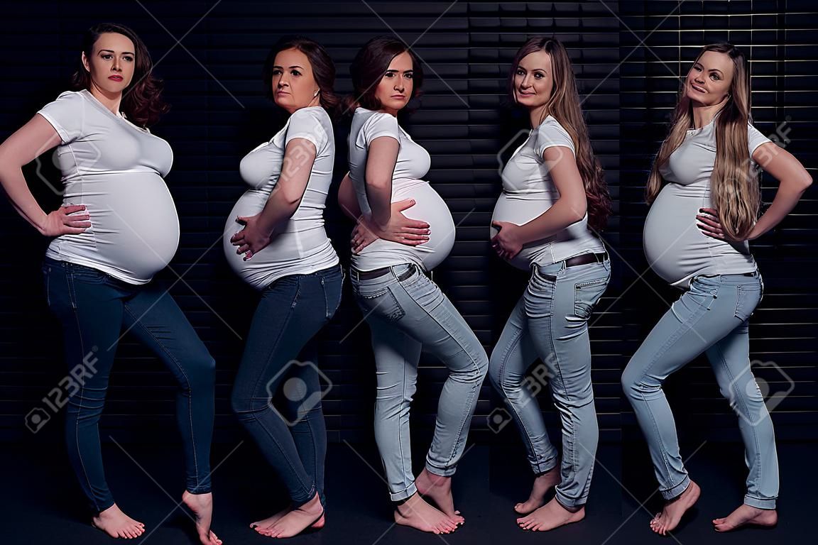 Pregnant women in white shirts and jeans on black background.
