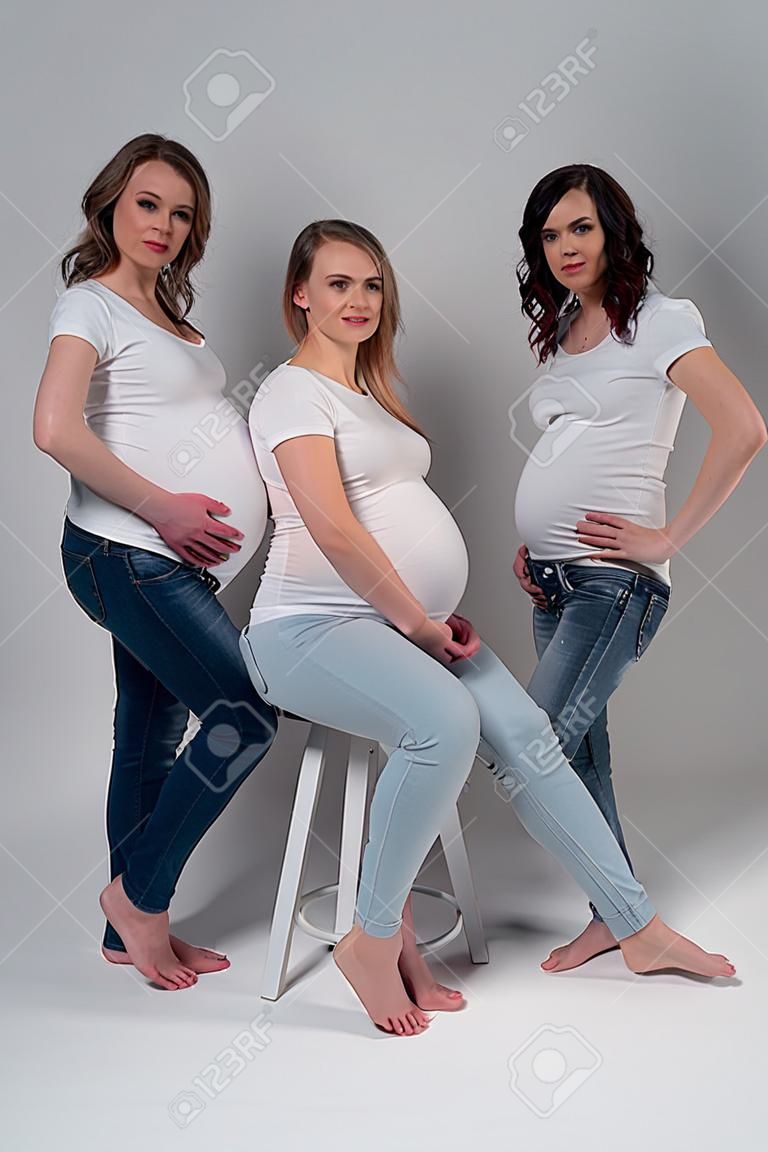 스튜디오에서 흰색 티셔츠와 청바지를 입은 세 명의 임산부.