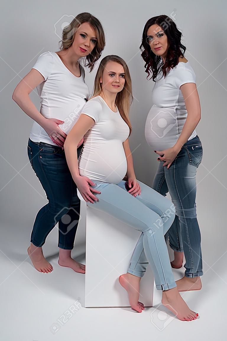 스튜디오에서 흰색 티셔츠와 청바지를 입은 세 명의 임산부.
