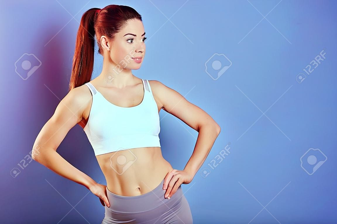 Portrait d'une jeune sportive caucasienne sportive et mince portant un soutien-gorge de sport blanc, debout avec les mains sur les hanches, regardant de côté, a une queue de cheval, copiez l'espace pour la publicité.