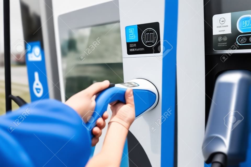 Man taking a fast EV charger from EV charging station in focus. Fast EV charger station. Electric vehicle charging. Alternative energy. AC car charger.
