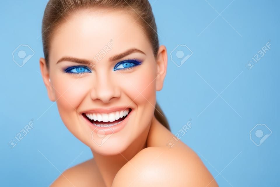 Close-up di una bella donna dagli occhi blu mostrando i suoi denti bianchi e sani Giovane modello femminile caucasica con largo sorriso perfetto su sfondo blu