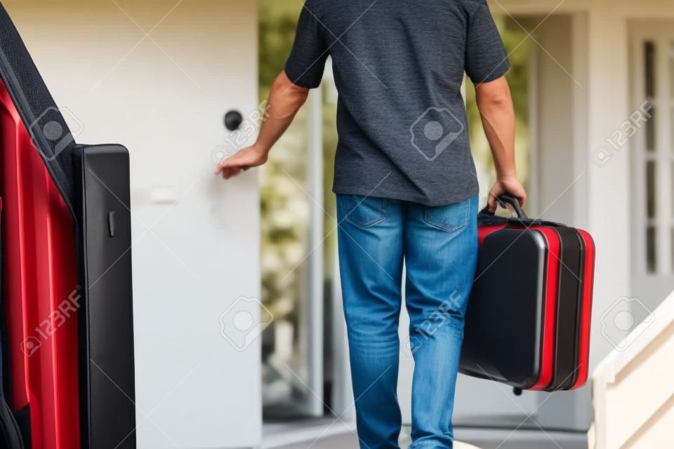 Ein Mann mit einem Koffer über den Fuß aus der Tür seines Hauses zu reisen