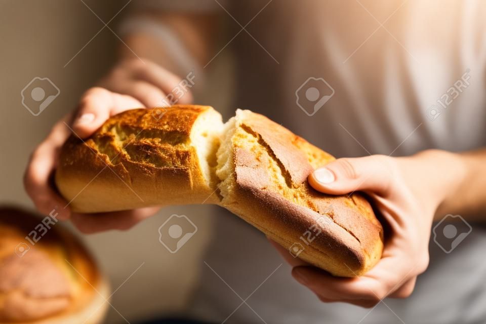 Męskie dłonie łamiące świeżo upieczony chleb, zbliżenie