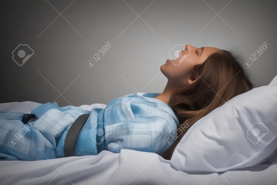 Schreeuwende meisje gebonden met riem in bed. Slaapverlamming concept