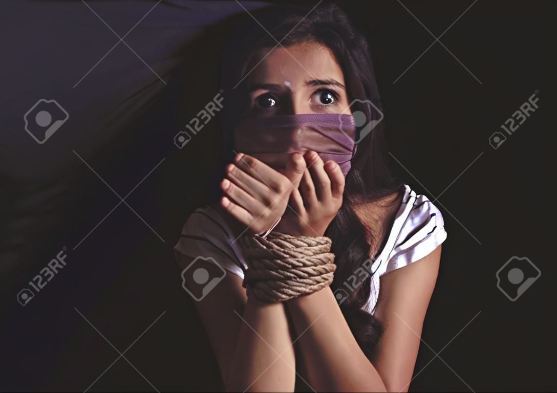 Young woman with tied hands subjected to violence in darkness