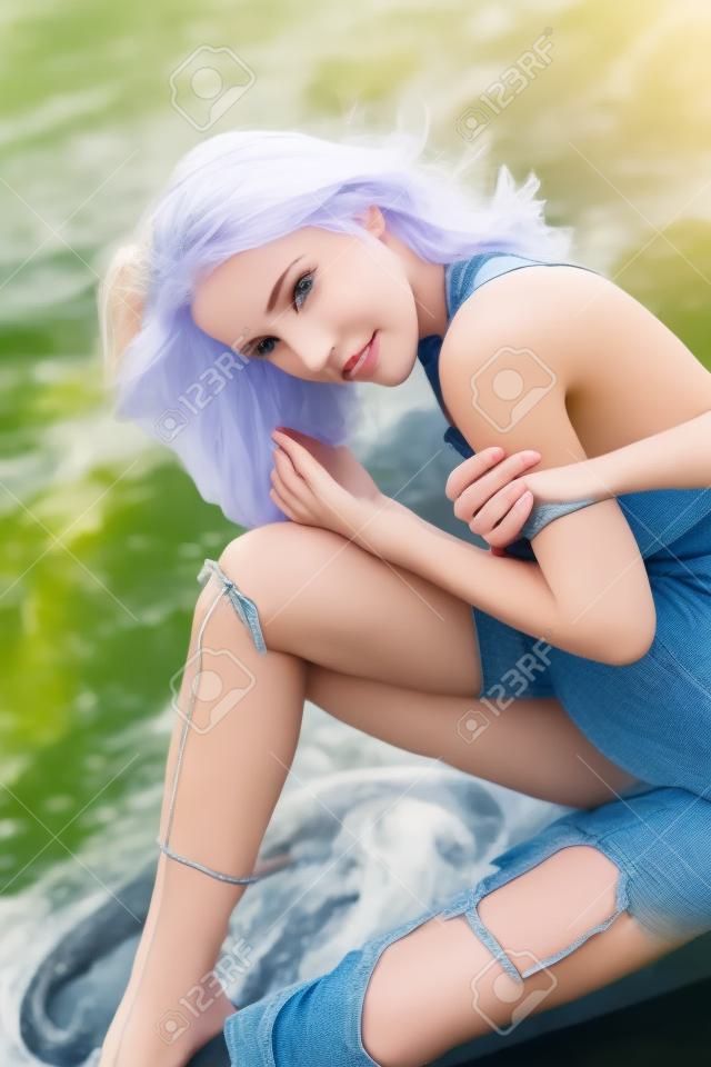Mujer joven de moda sentada en la orilla del río