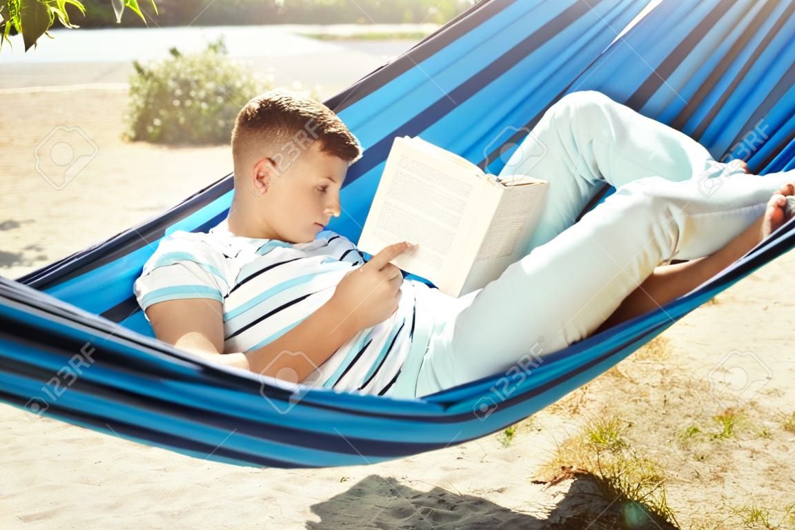 Młody człowiek czyta książkę podczas odpoczynku w hamaku na świeżym powietrzu