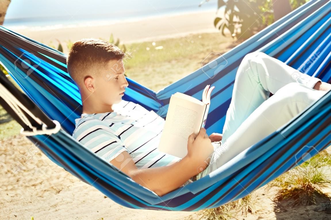 Młody człowiek czyta książkę podczas odpoczynku w hamaku na świeżym powietrzu