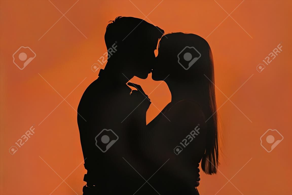 Dark silhouette of young romantic couple kissing against color background