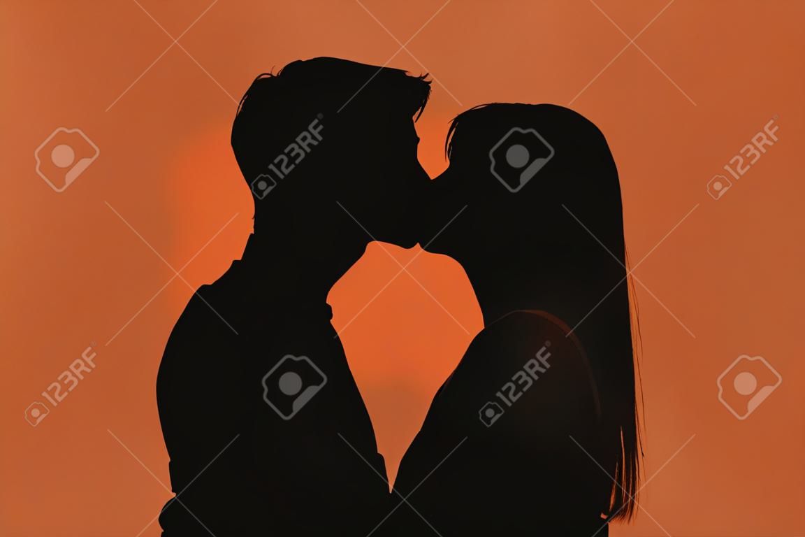 Silhouette sombre du jeune couple romantique s'embrassant sur un fond de couleur
