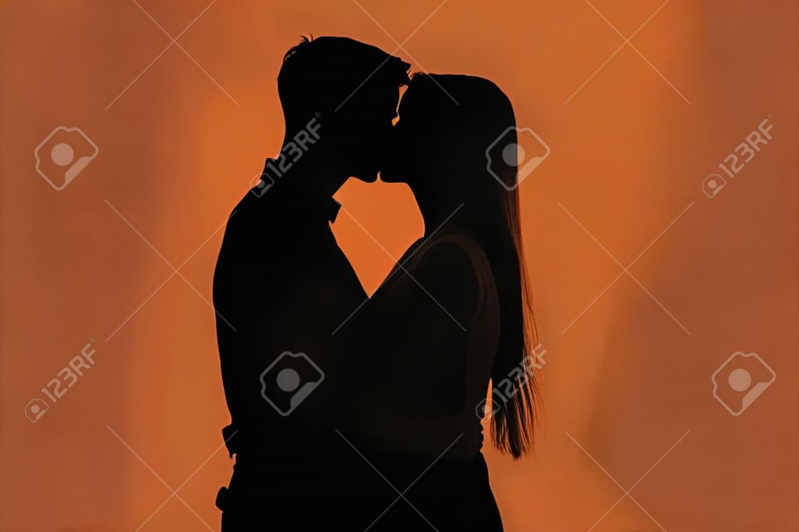 Silueta oscura de la joven pareja romántica besándose contra el fondo de color