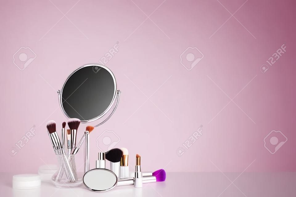 Set of makeup cosmetics with brushes and mirror on table