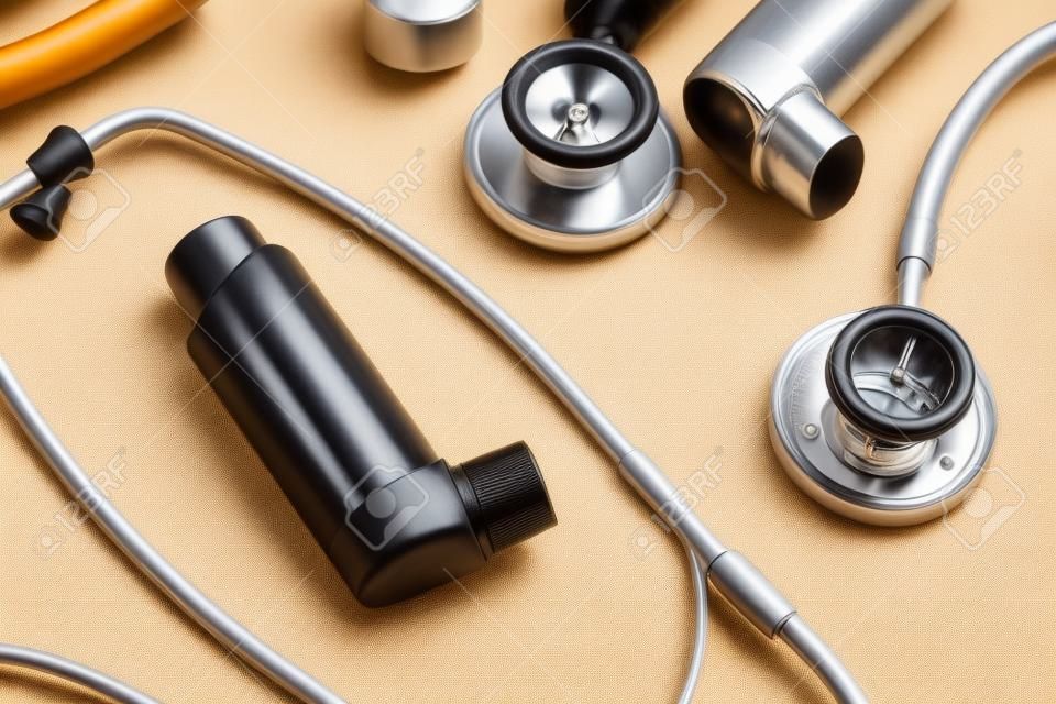 Asthma inhalers and stethoscopes on beige background, closeup