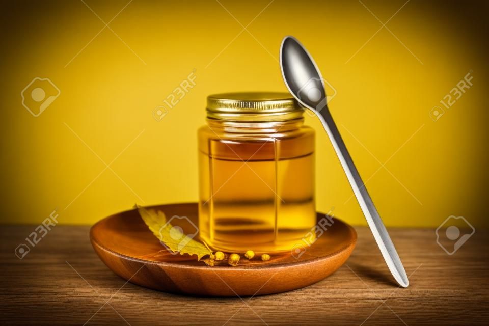 Piatto di legno con barattolo di gustoso sciroppo d'acero e cucchiaio su sfondo giallo