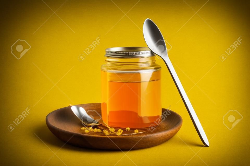Wooden plate with jar of tasty maple syrup and spoon on yellow background