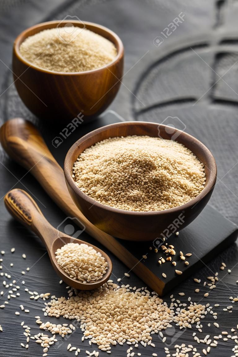 Wooden spoon and bowls of sesame seeds on dark background