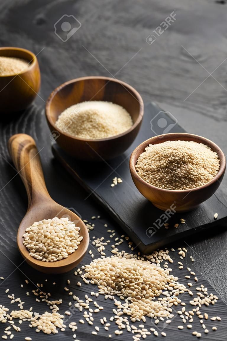 Wooden spoon and bowls of sesame seeds on dark background