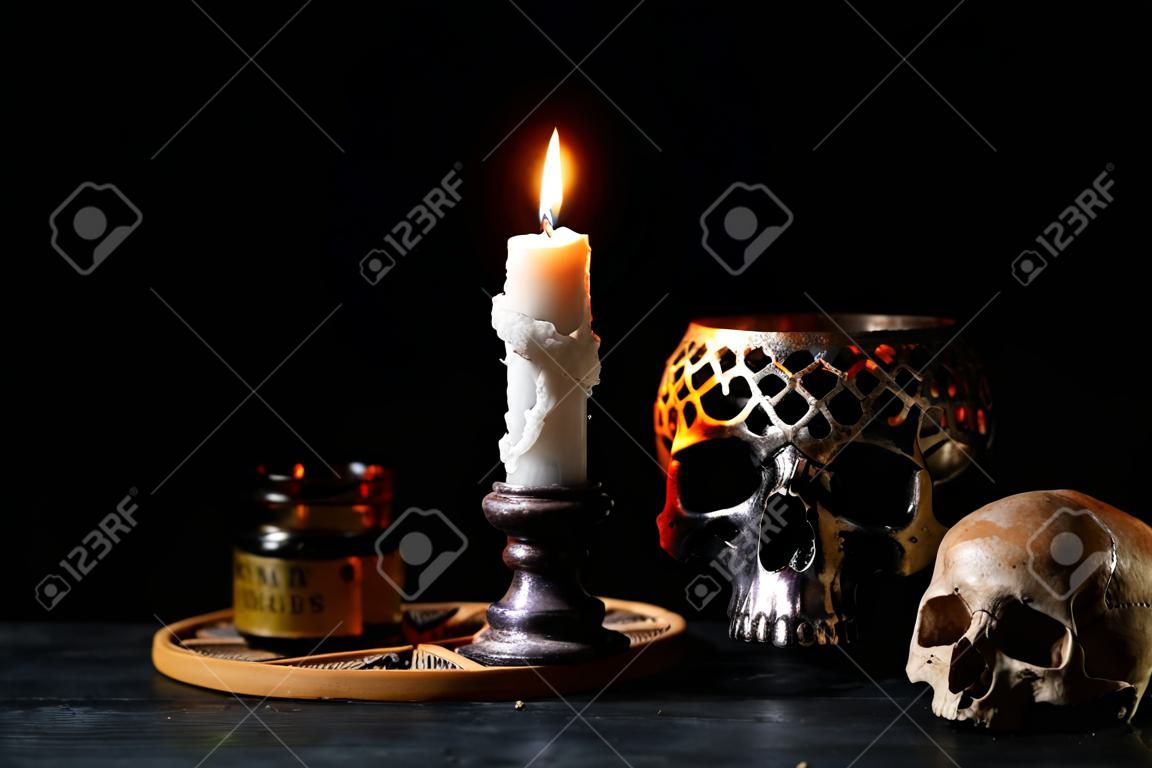 Burning candle, scull and magic attributes for ritual on dark background