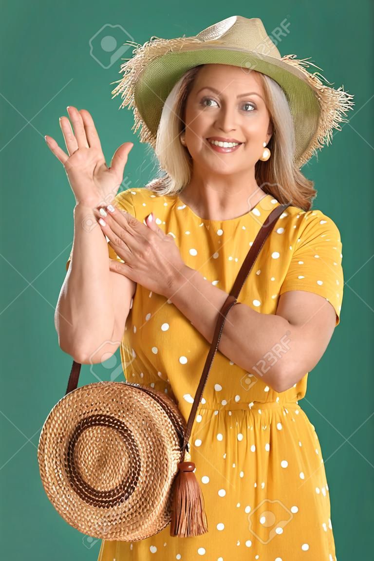 Glückliche reife Frau mit Strohhut und stylischer Tasche auf grünem Hintergrund