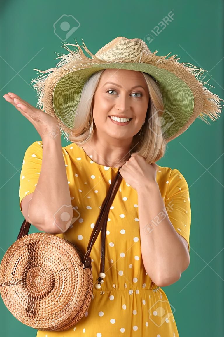 Glückliche reife Frau mit Strohhut und stylischer Tasche auf grünem Hintergrund