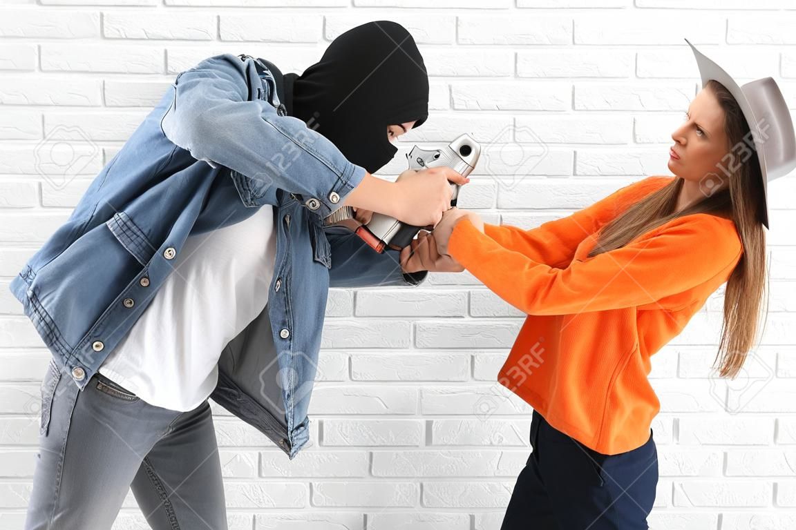 Young woman with pepper spray defending herself against thief on white brick background