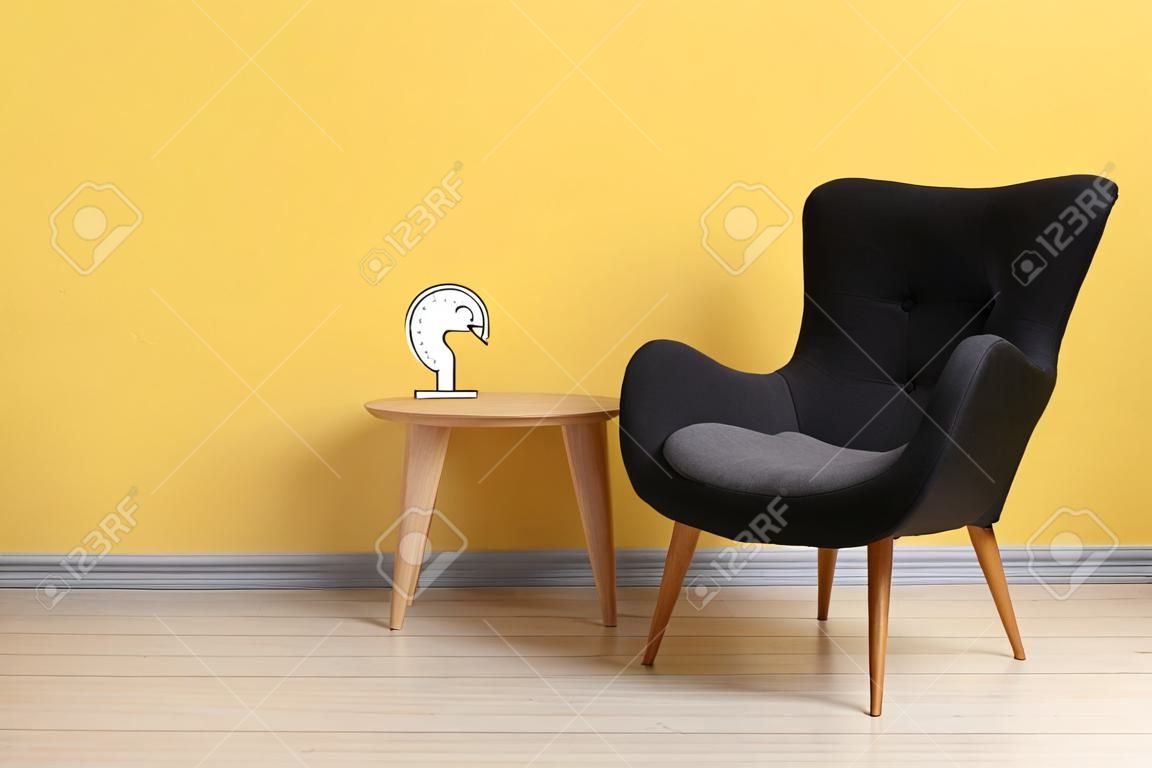 Stylish gray armchair and table near yellow wall