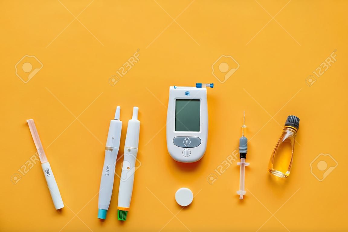 Blutzuckermessgerät mit Lanzettenstift, Insulin und Spritzen auf orangefarbenem Hintergrund. Diabetes-Konzept