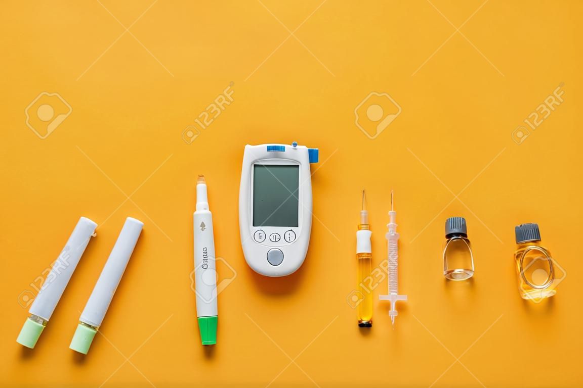 주황색 배경에 란셋 펜, 인슐린, 주사기가 있는 글루코미터. 당뇨병 개념
