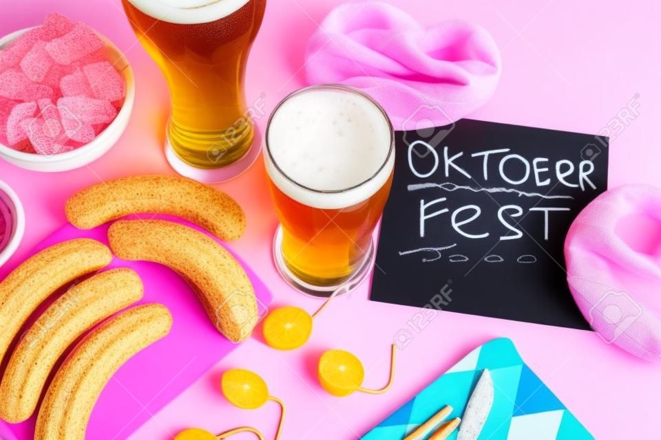 Glasses of cold beer, chalkboard with word and different snacks on pink background