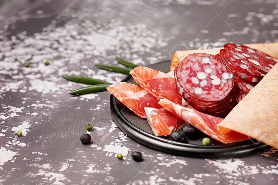 Grid with slices of tasty salami on gray background