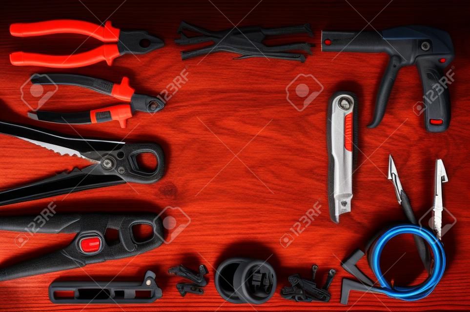 Professional electrician tools on light wood background. All tools with red elements. Pliers, gloves. connectors, multimeter probe. top view. Place for text or logotype in center.